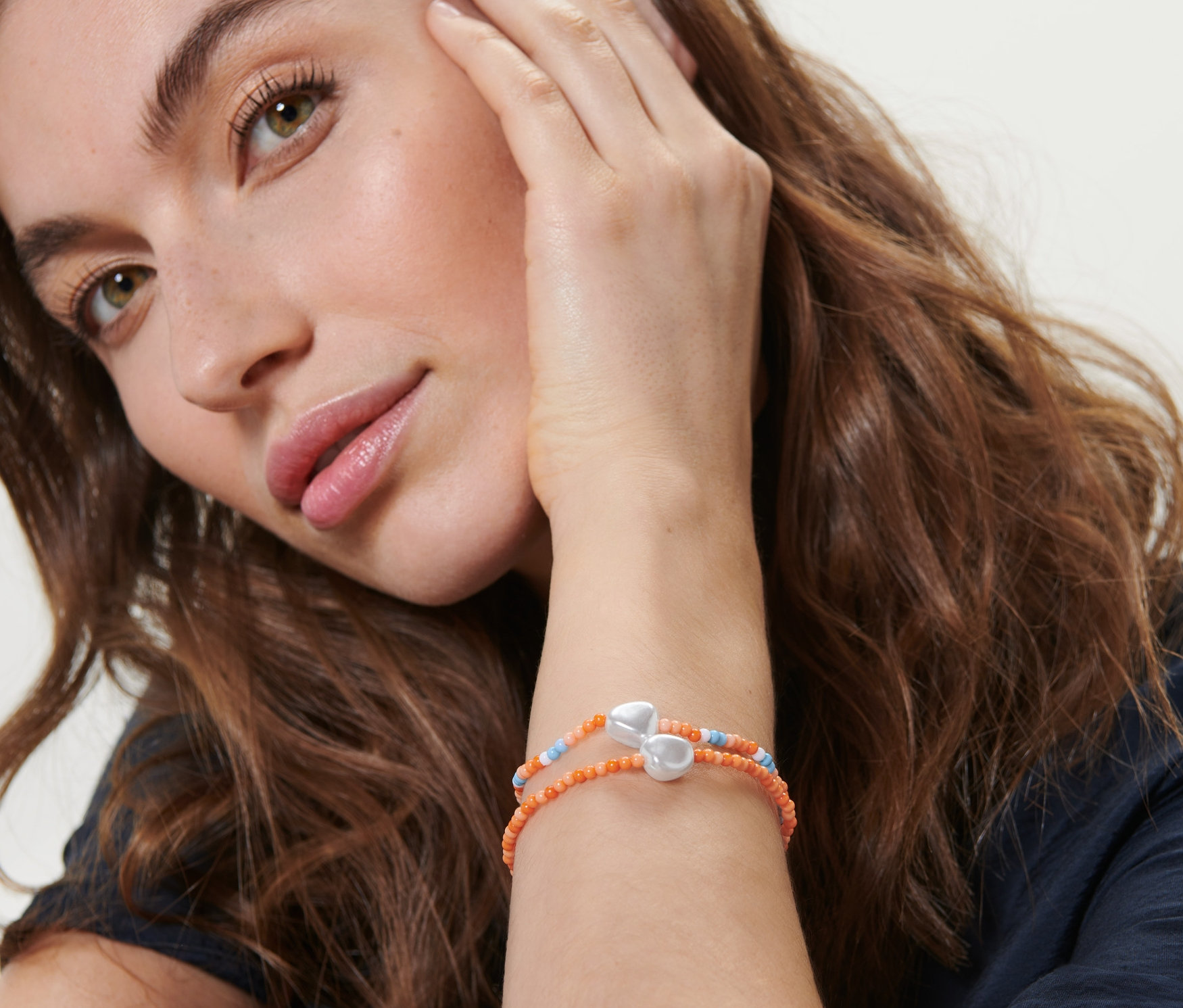 Kobieta dotyka twarzy, na nadgarstku ma założone 2 bransoletki.