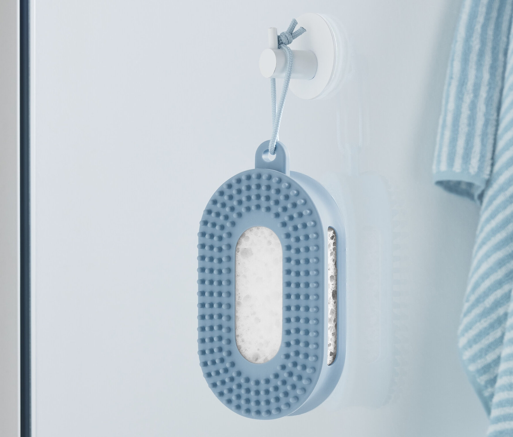 Niebieska gąbka pod prysznic wisi na ścianie obok paskowanego ręcznika.