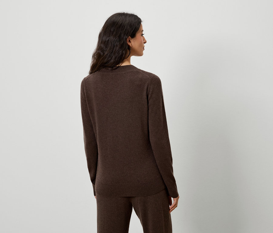 Kobieta pozuje w brązowym swetrze i spodniach.