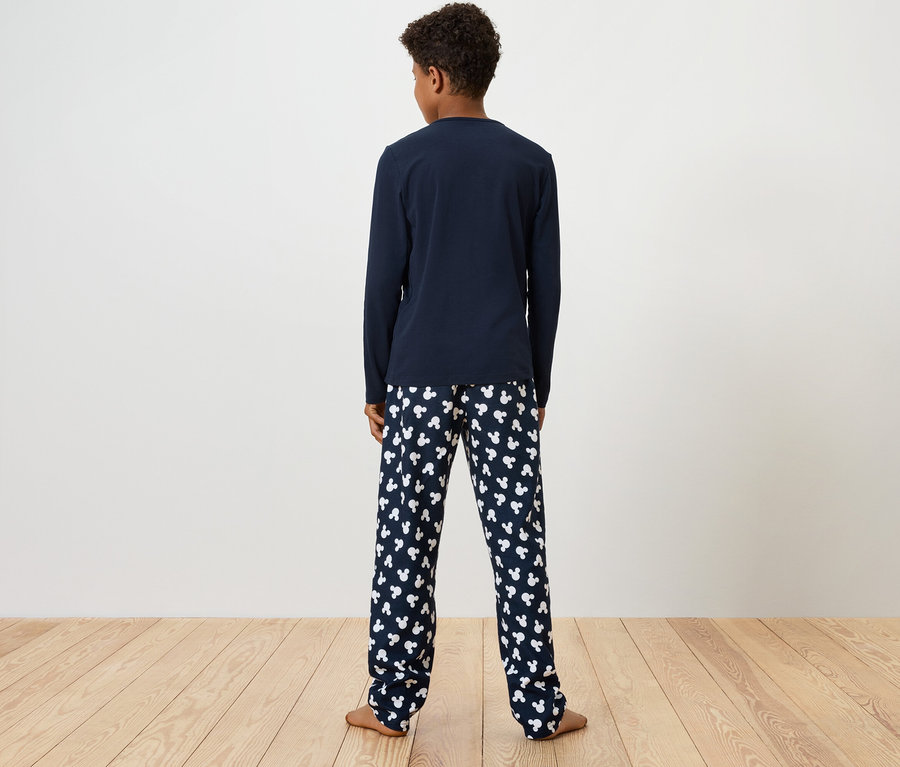 Chłopiec stoi tyłem do kamery, ma na sobie niebieską koszulkę piżamową z długim rękawem i spodnie piżamowe z nadrukiem białych misiów.