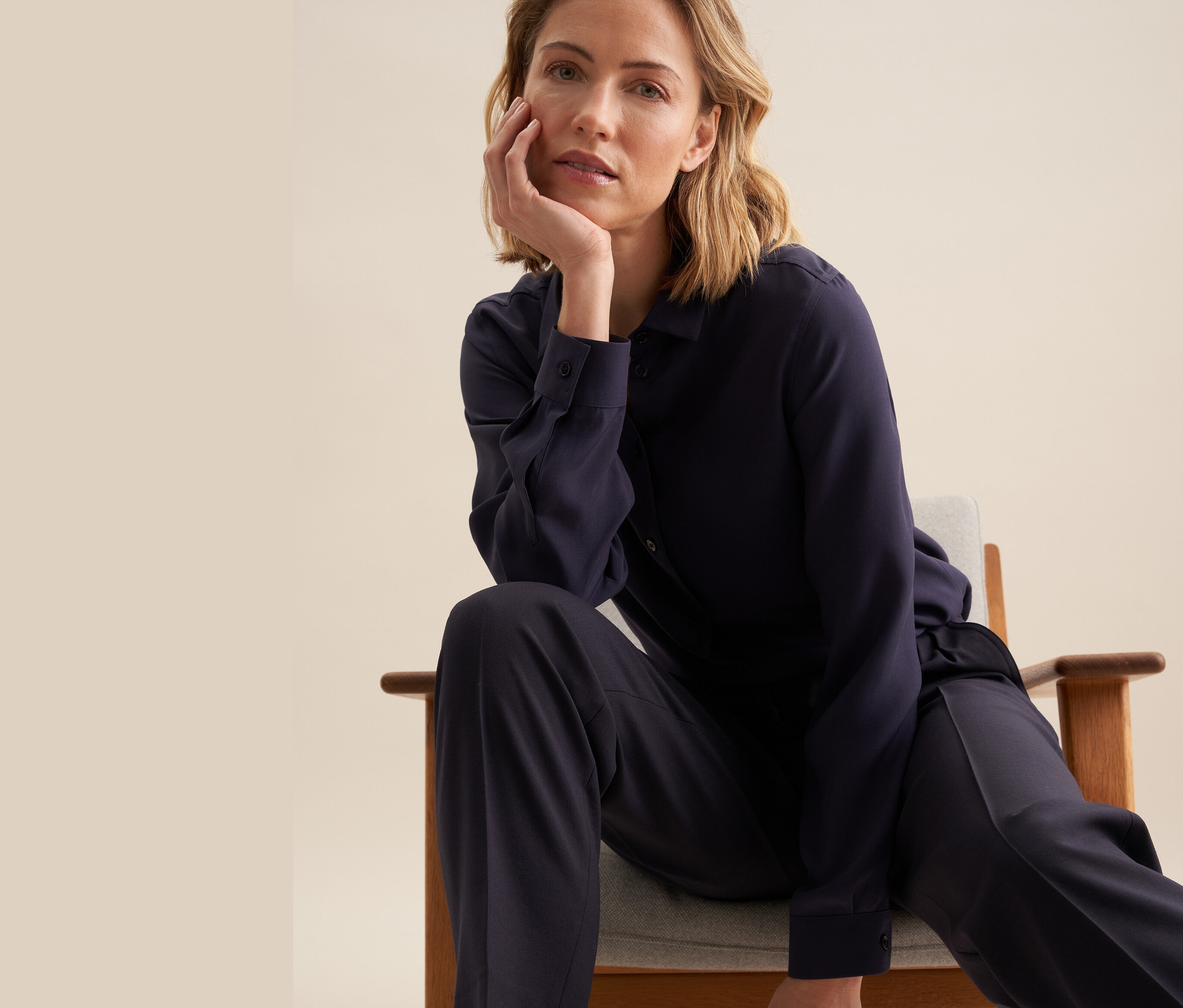 Kobieta siedzi na krześle, ubrana w koszulę z wiskozy Seidensticker.