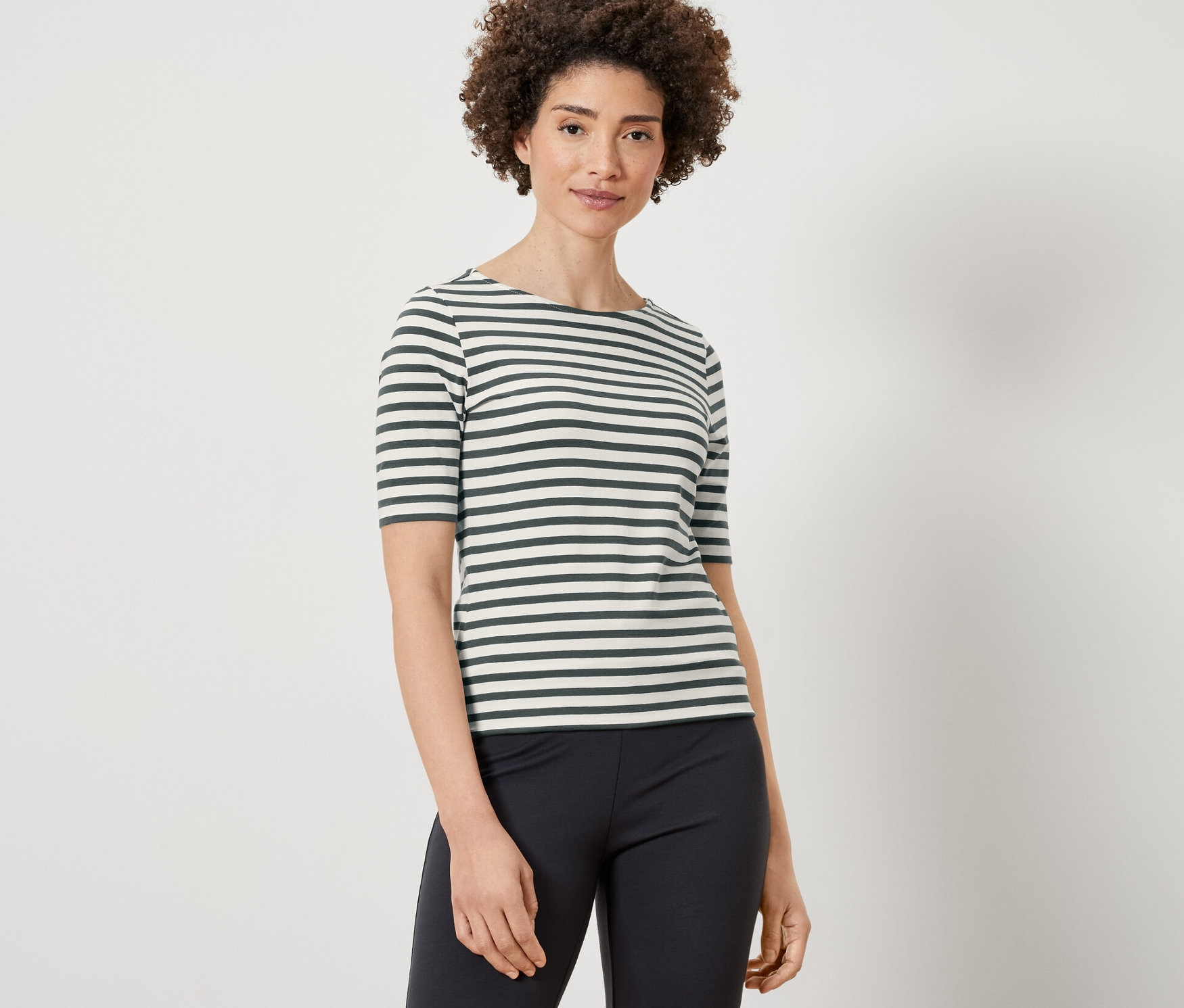 Kobieta ma na sobie koszulkę z półdługim rękawem w zielone paski i czarne spodnie.