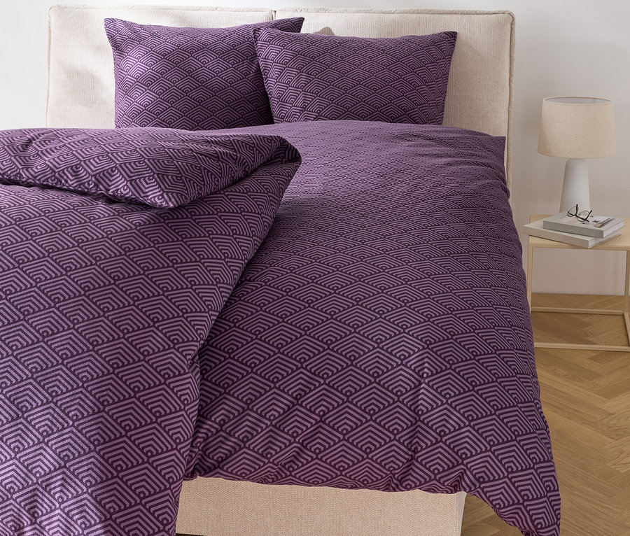 Łóżko z fioletową geometryczną pościelą i dwiema poduszkami.