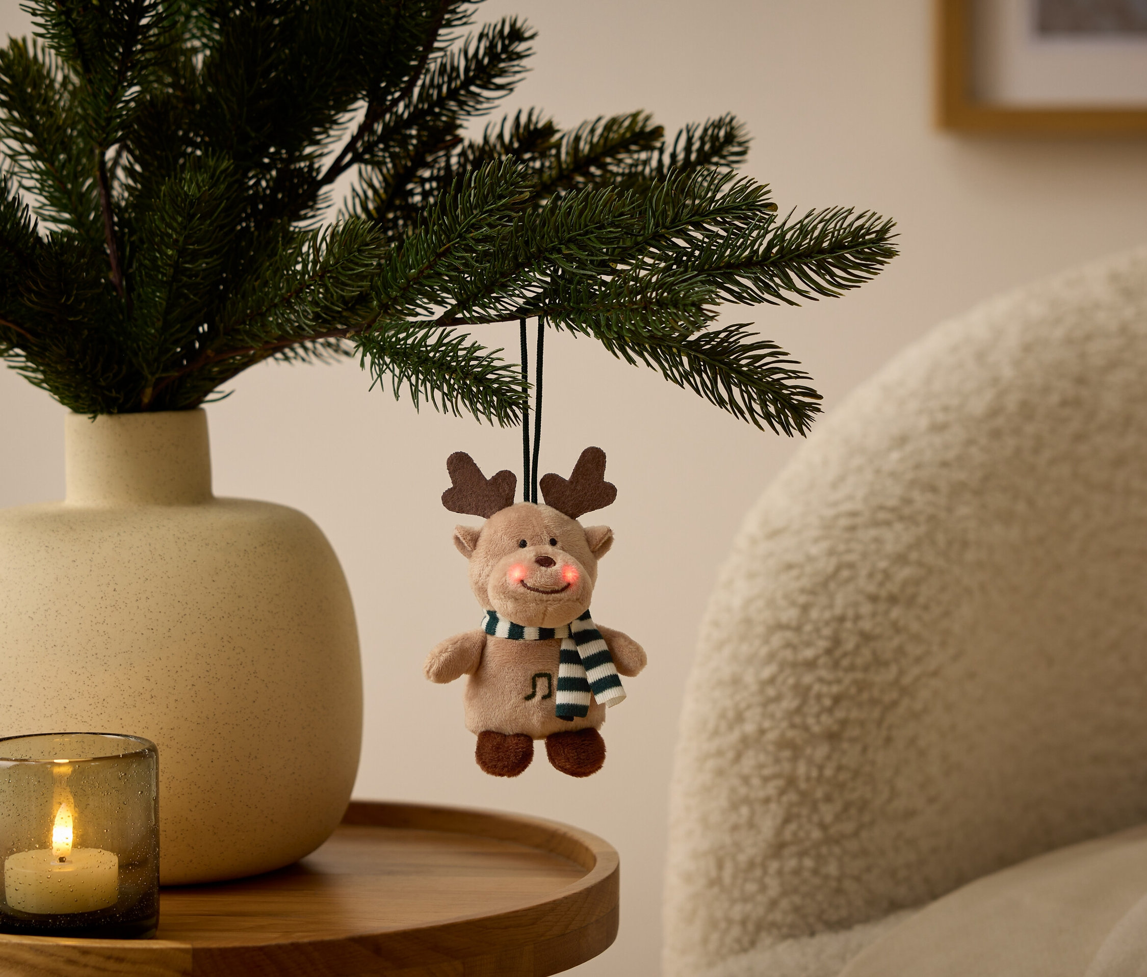 Ozdoba renifera wisi na gałęzi w wazonie obok świecy na stole.