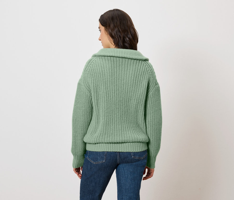 Kobieta w zielonym swetrze patrzy w lewo.