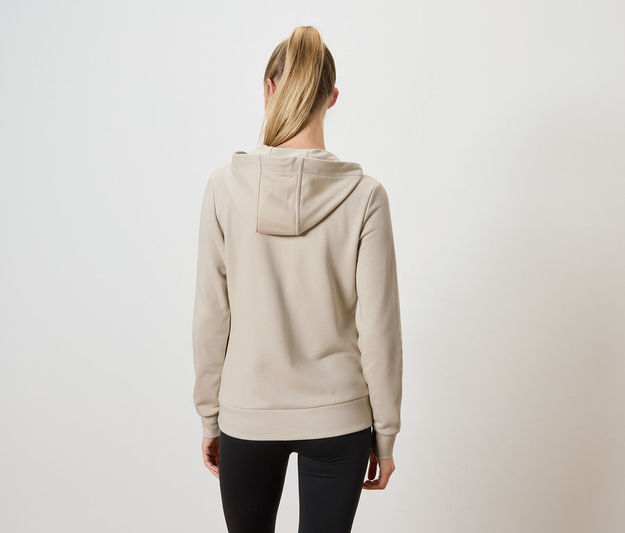 Widok z tyłu kobiety z blond włosami związanymi w koński ogon, ubranej w beżową bluzę z kapturem i czarne spodnie.