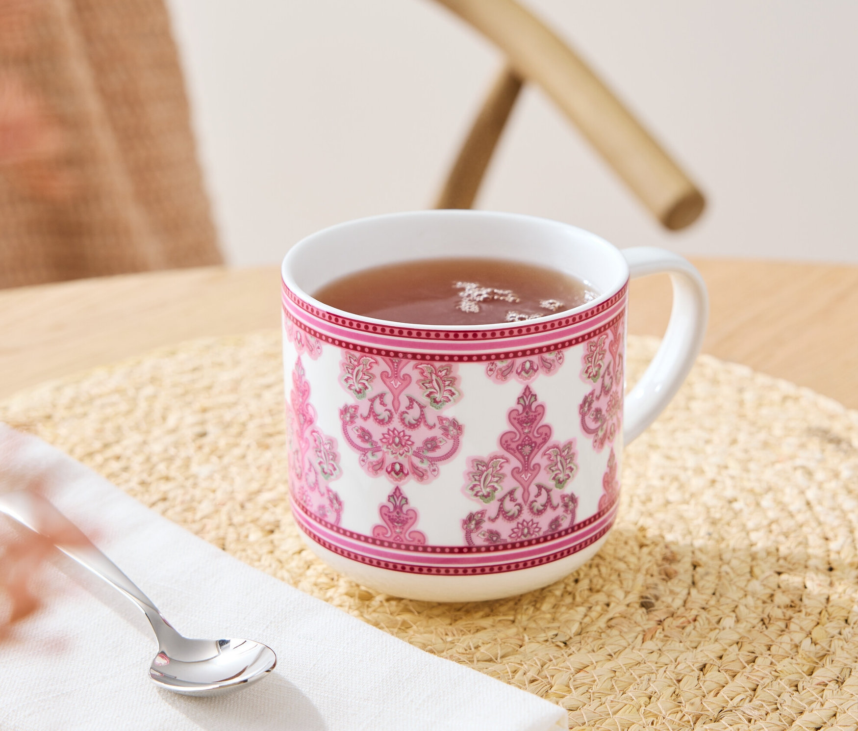 Na stole stoi kubek z napojem, obok leży łyżeczka na serwetce.