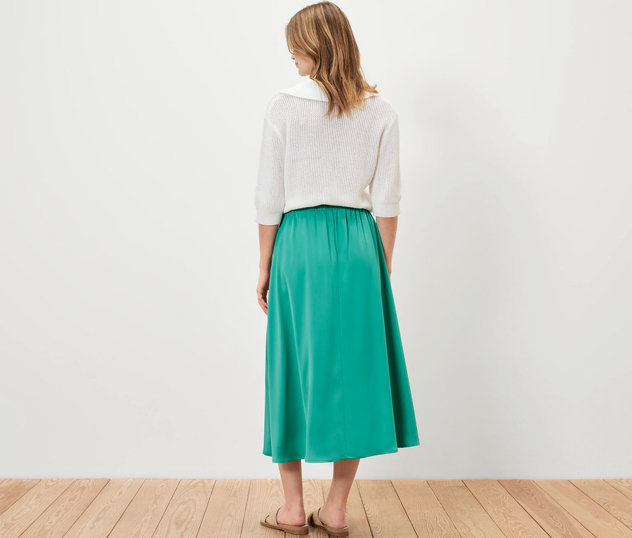 Kobieta stojąca tyłem ma na sobie spódnicę z satyny.