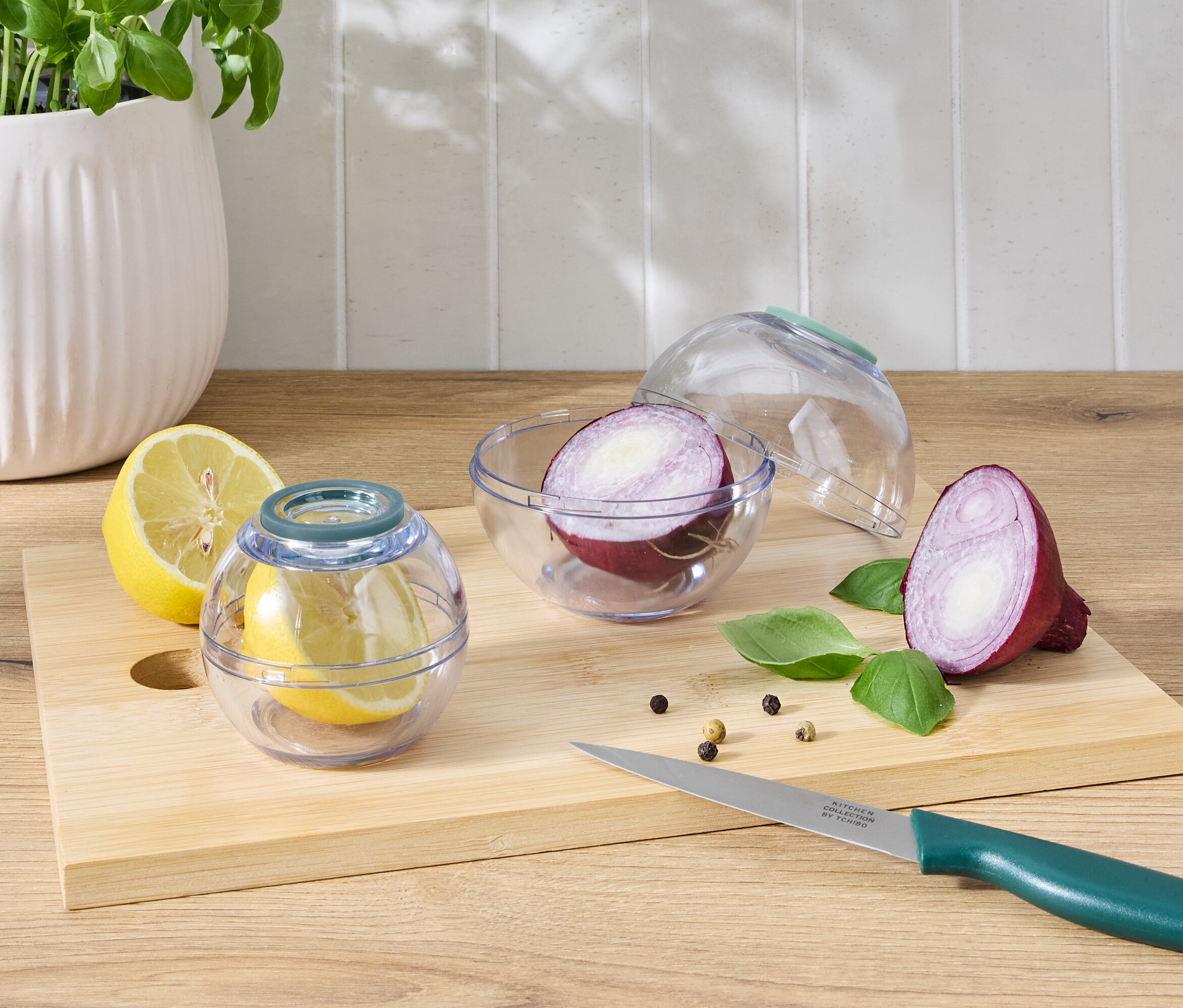 Połówka cytryny w przezroczystym pojemniku obok połówki cytryny i połówki czerwonej cebuli w przezroczystym pojemniku obok połówki czerwonej cebuli na desce do krojenia z nożem.