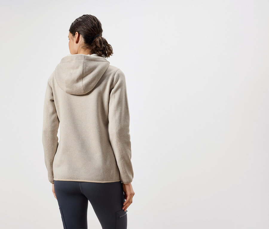 Z tyłu widać kobietę w beżowej bluzie z kapturem i granatowych spodniach.