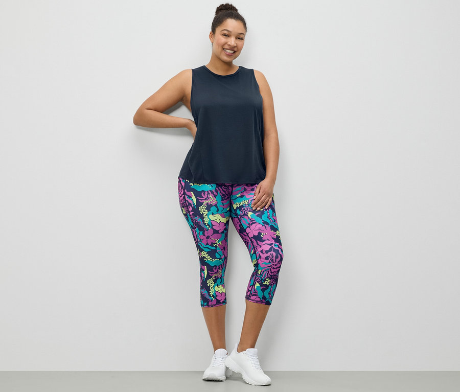Kobieta pozuje w granatowym topie sportowym i legginsach sportowych o długości 3/4 z wzorem na całej powierzchni.