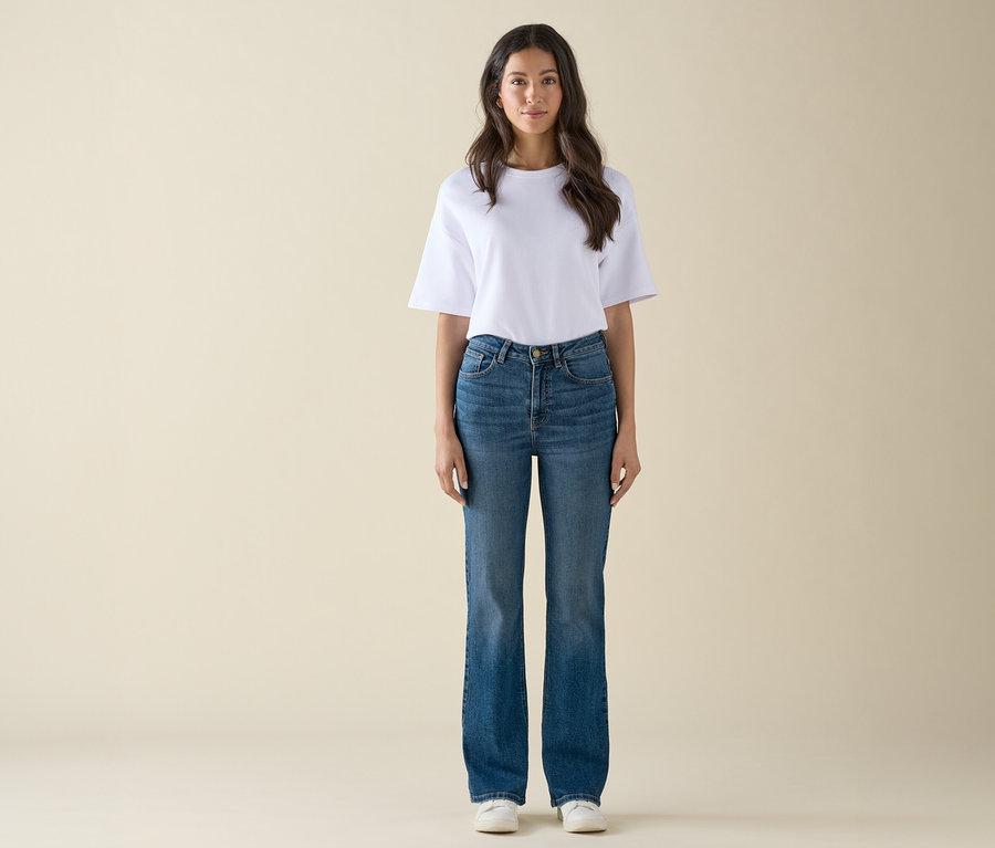 Kobieta stoi, ma na sobie białą koszulkę, niebieskie dżinsy i białe tenisówki.