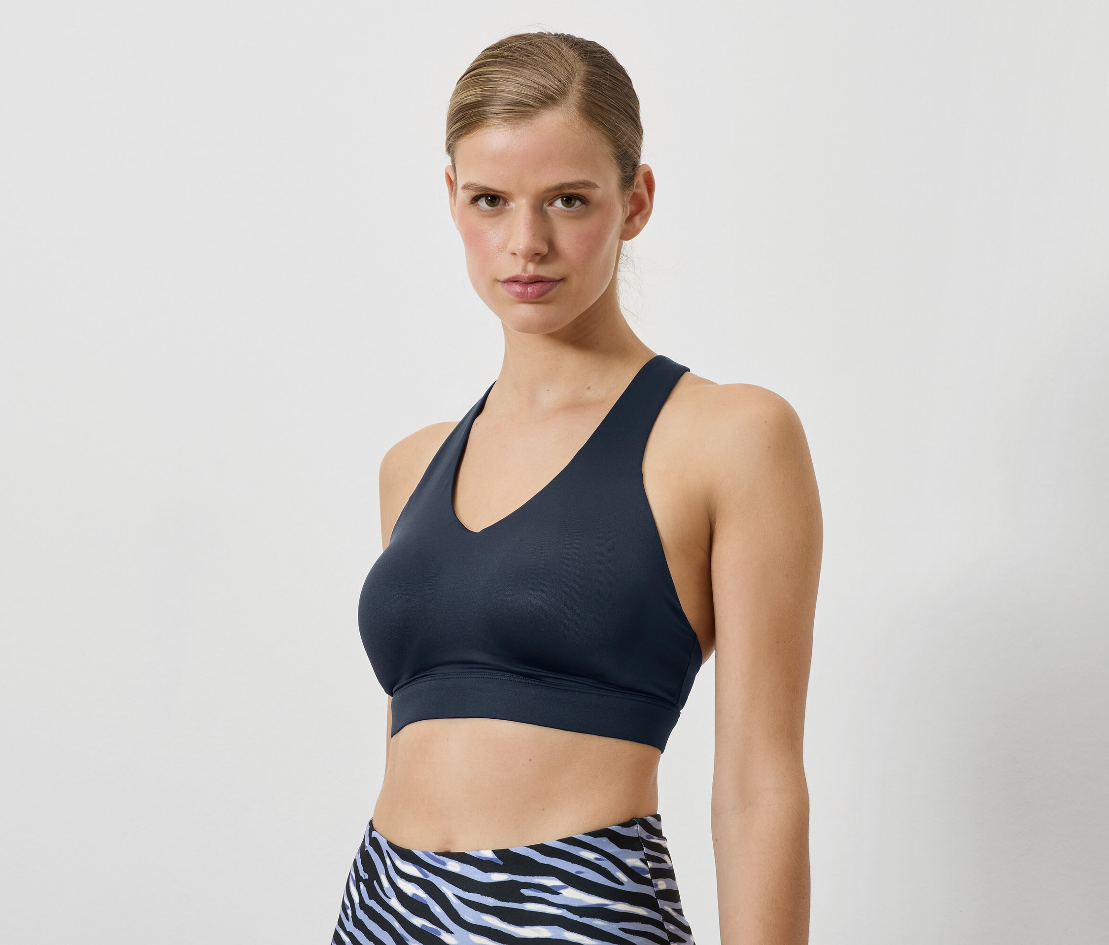 Kobieta ma na sobie granatowy biustonosz sportowy i legginsy we wzór zwierzęcy.
