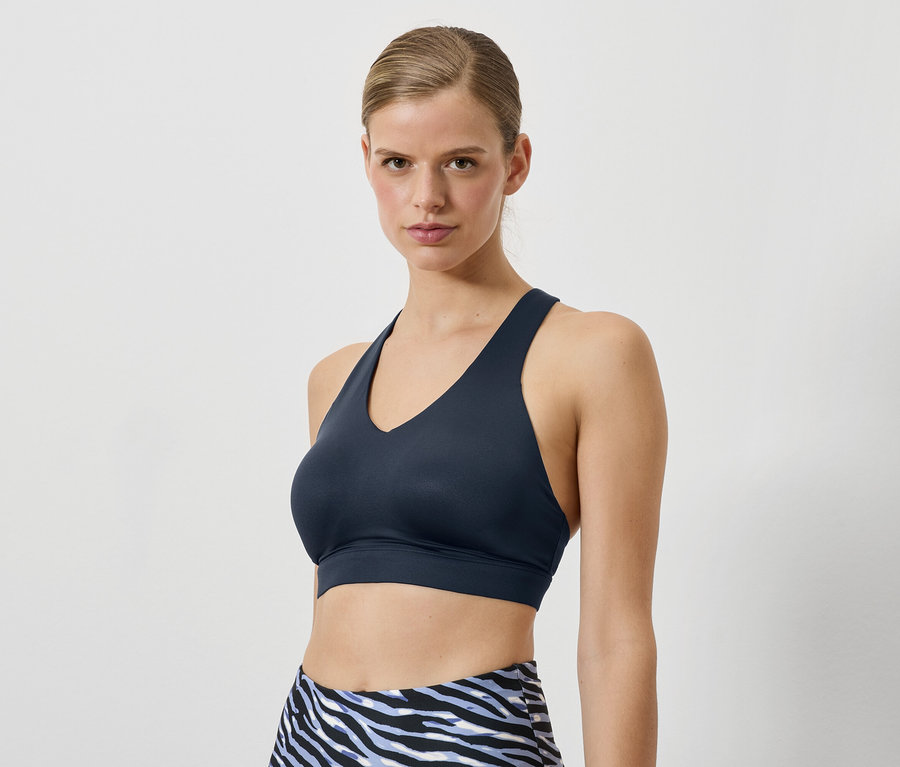 Kobieta ma na sobie granatowy biustonosz sportowy i legginsy we wzór zwierzęcy.