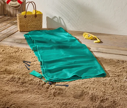 Zielony ręcznik plażowy leży na piasku obok żółtych okularów do nurkowania i koszyka.