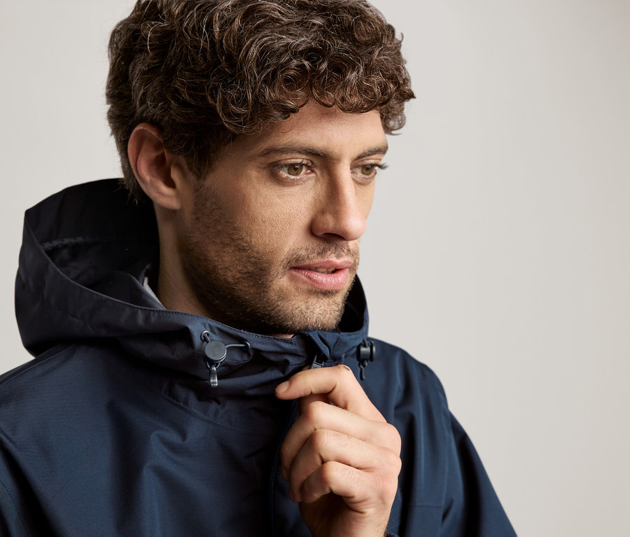 Mężczyzna o kręconych włosach w granatowej kurtce z kapturem.