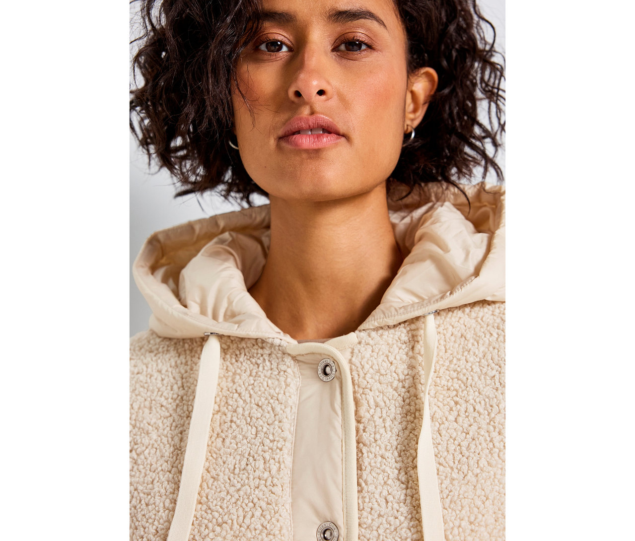 Kobieta ma na sobie bezową bluzę pluszową z odpinanym kapturem Street One.