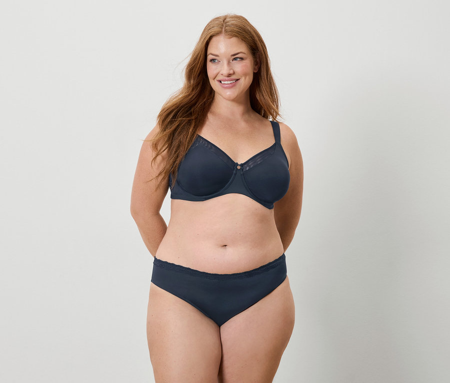 Uśmiechnięta kobieta z długimi rudymi włosami w granatowym biustonoszu i majtkach.