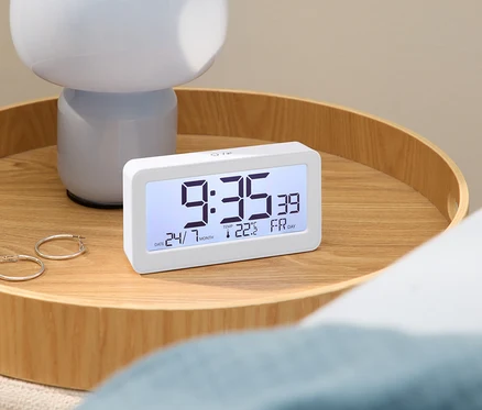 Cyfrowy budzik z godziną 9:35 na drewnianym stole z lampą i kolczykami.