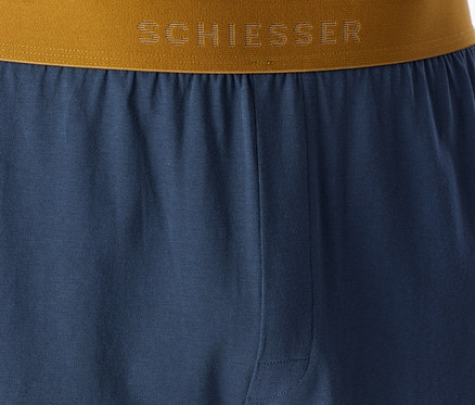 Niebieskie spodnie piżamowe z brązowo-złotym pasem, na którym widnieje logo „SCHIESSER”.