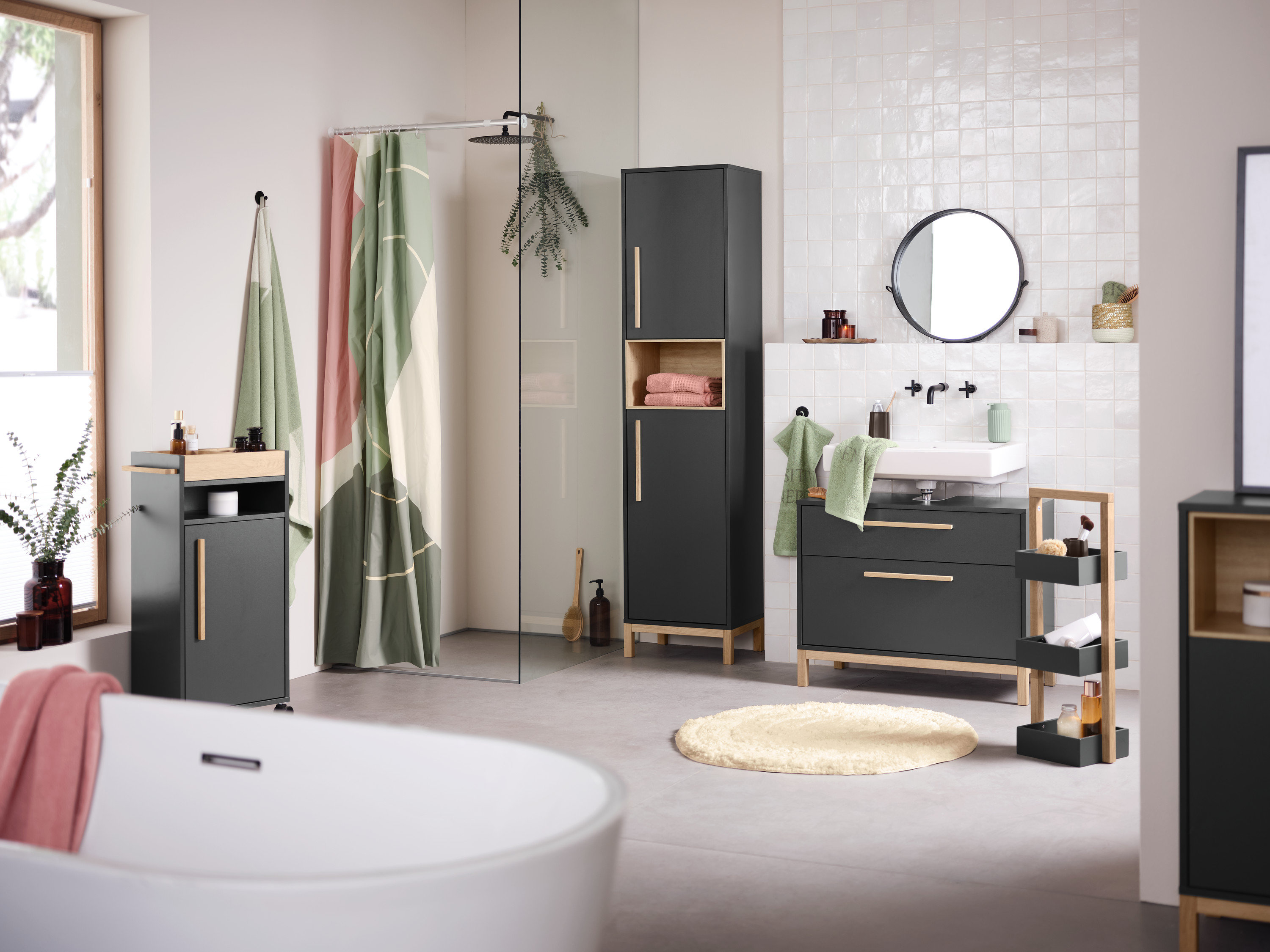 Wnętrze łazienki z umywalką, lustrem i antracytowymi szafkami łazienkowymi Eklund. Na pierwszym planie wanna.