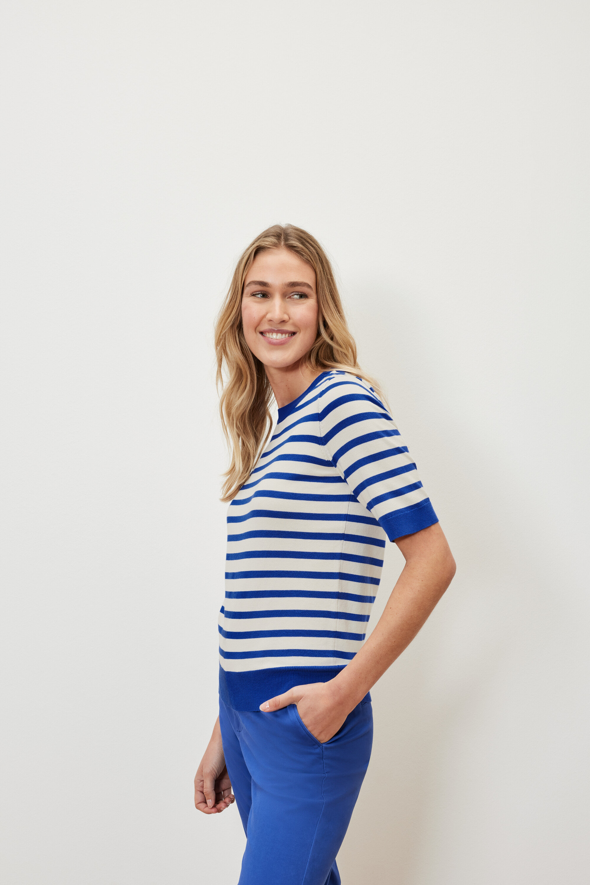 Kobieta ma na sobie cienki sweter w paski i niebieskie spodnie.