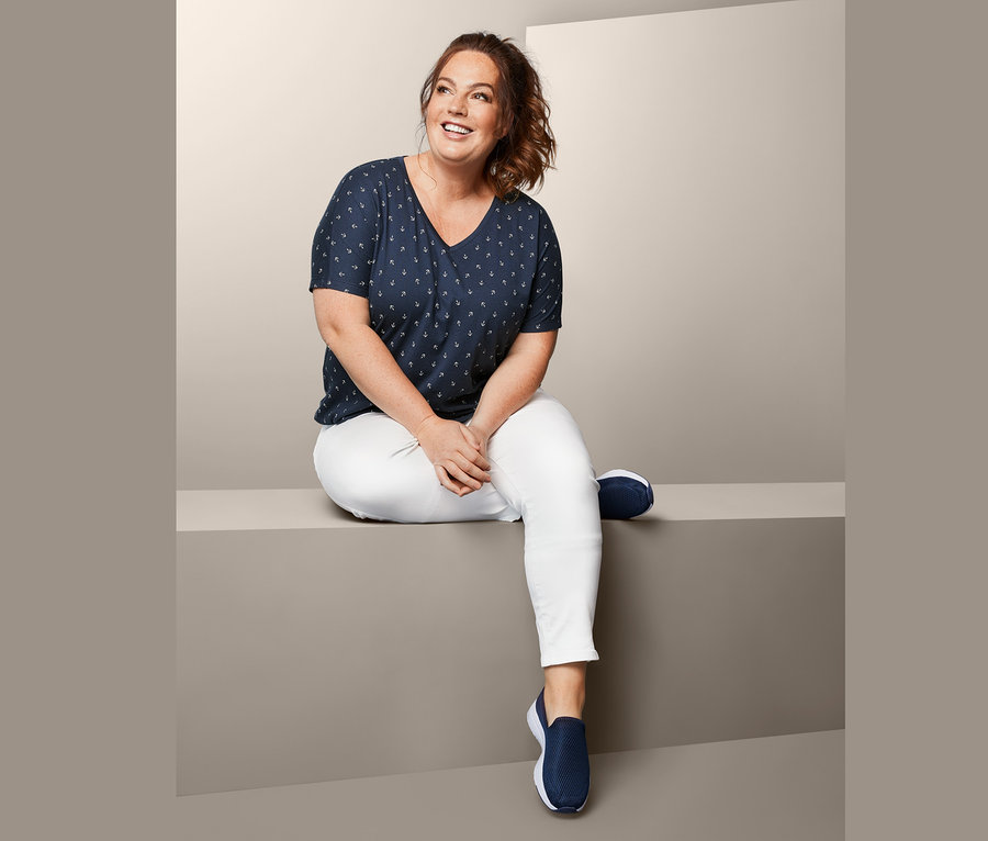 Kobieta siedzi i ma na sobie spodnie damskie o długości do kostek i bluzkę.
