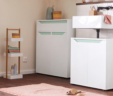 Wnętrze łazienki z szafką pod umywalkę, szafką łazienkową typu sideboard i wysoką szafką łazienkową. Regał stojący z 3 skrzynkami i tapicerowana ławka ze skrzynią na kółkach.