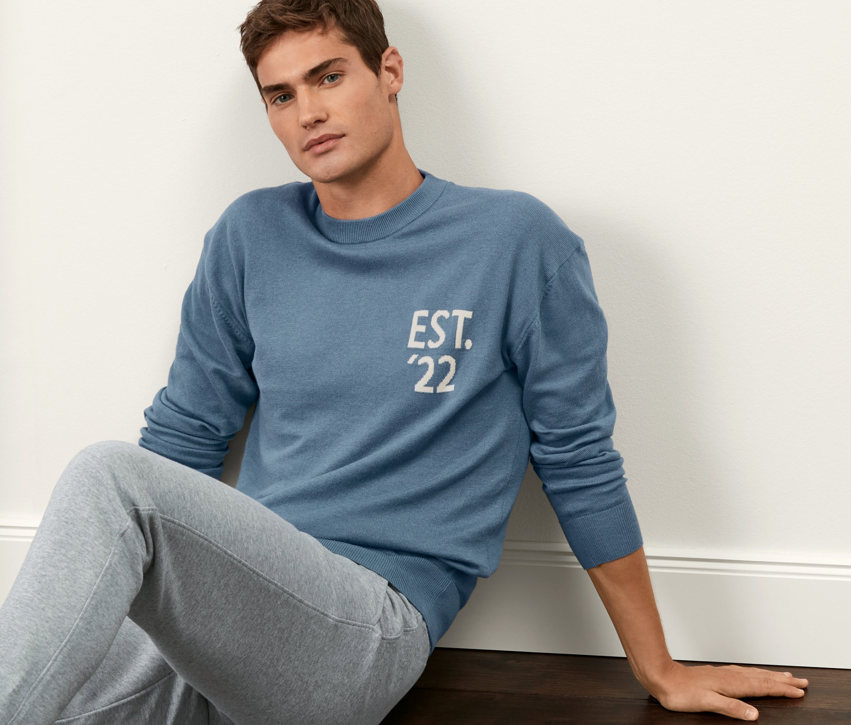 Mężczyzna siedzi na podłodze i ma na sobie niebieski sweter.