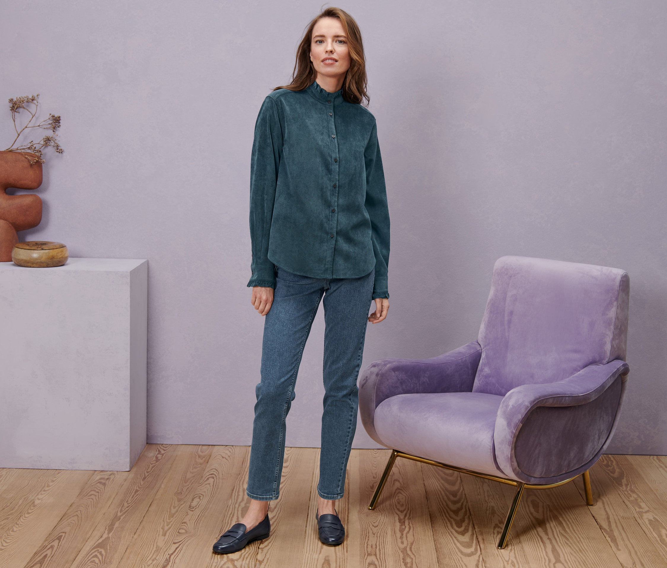 Kobieta stoi ubrana w jeansy Straight »Fit Juna«, mid blue, bluzkę sztruksową z falbanką i półbuty skórzane.