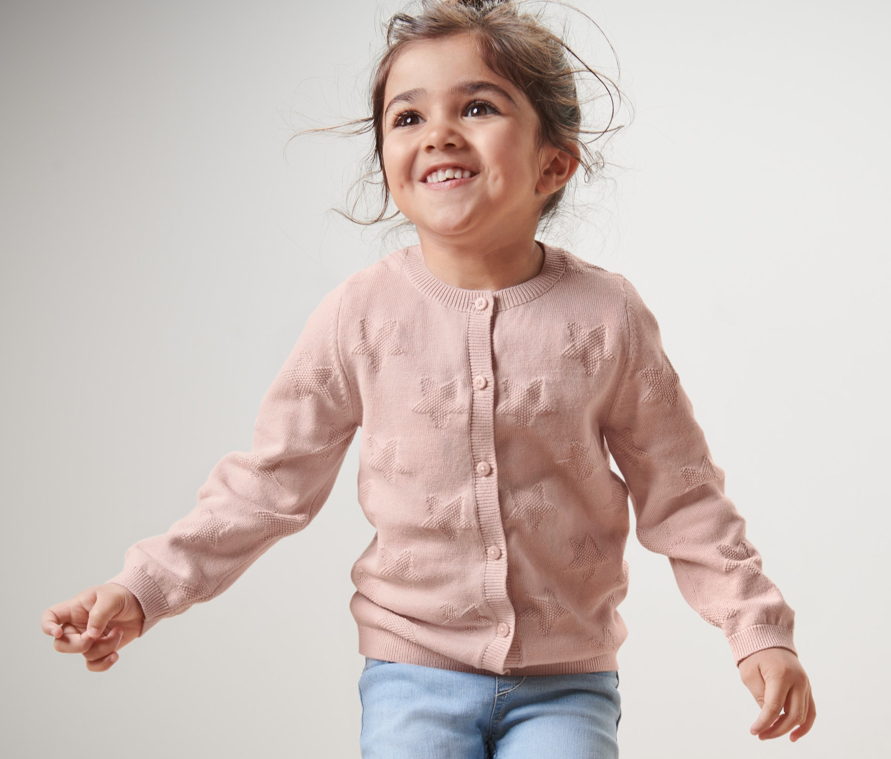 Uśmiechnięta dziewczyna ma na sobie dziecięcy sweter z dzianiny i dżinsy.
