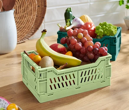 Zielona składana skrzynka do przechowywania z bananem, jabłkiem, kiwi i winogronami. W tle zielona składana skrzynka do przechowywania z warzywami.