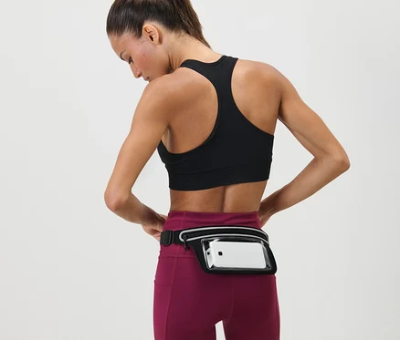 Kobieta dopasowuje Pasek do biegania na smartfon wokół talii. Ma na sobie biustonosz sportowy i legginsy.