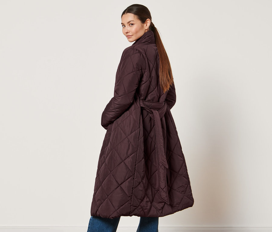 Kobieta patrzy przez ramię i ma na sobie płaszcz pikowany.