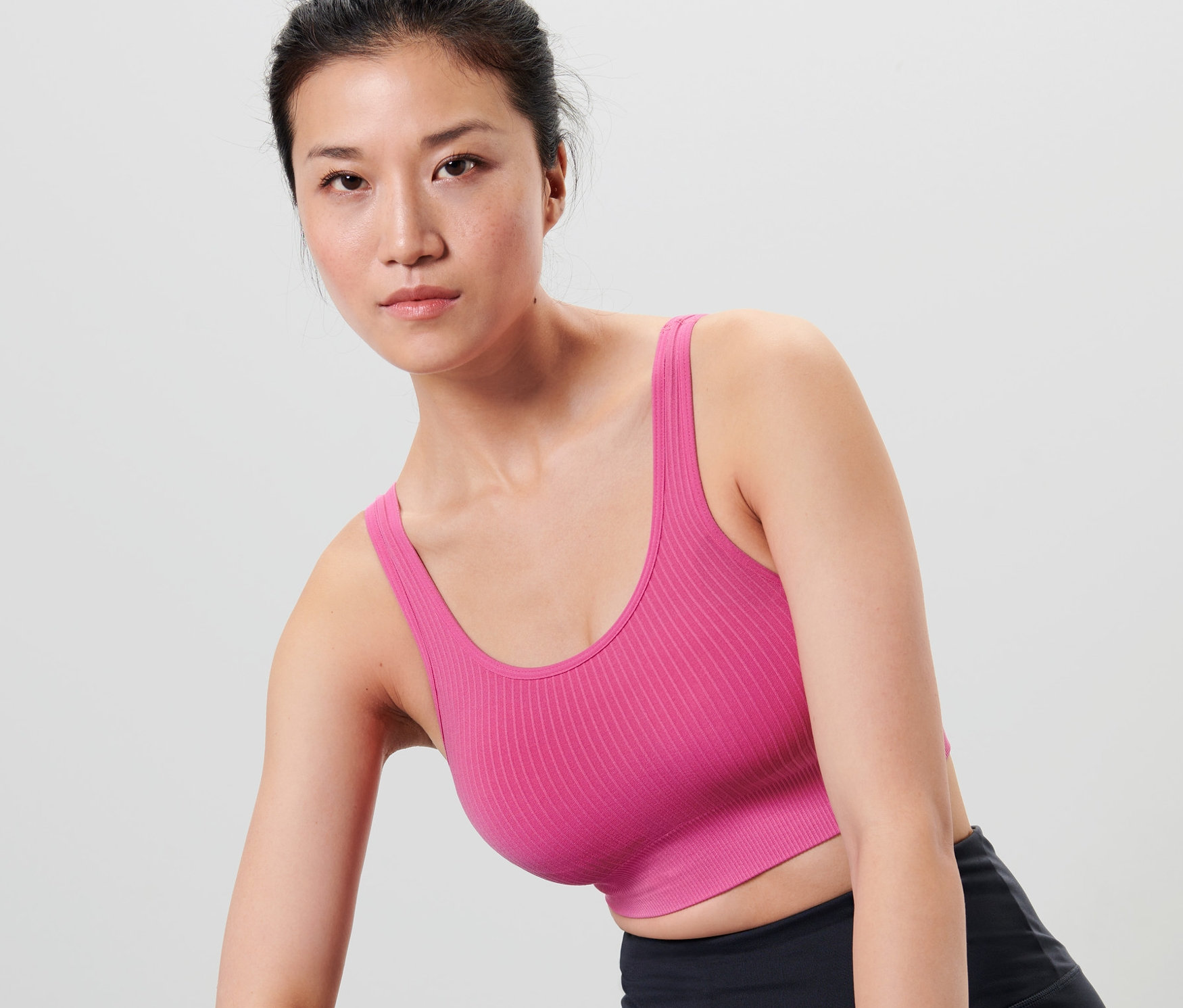 Azjatka ma na sobie bezszwowy biustonosz sportowy, czarne spodenki sportowe i fioletową opaskę na rękę.