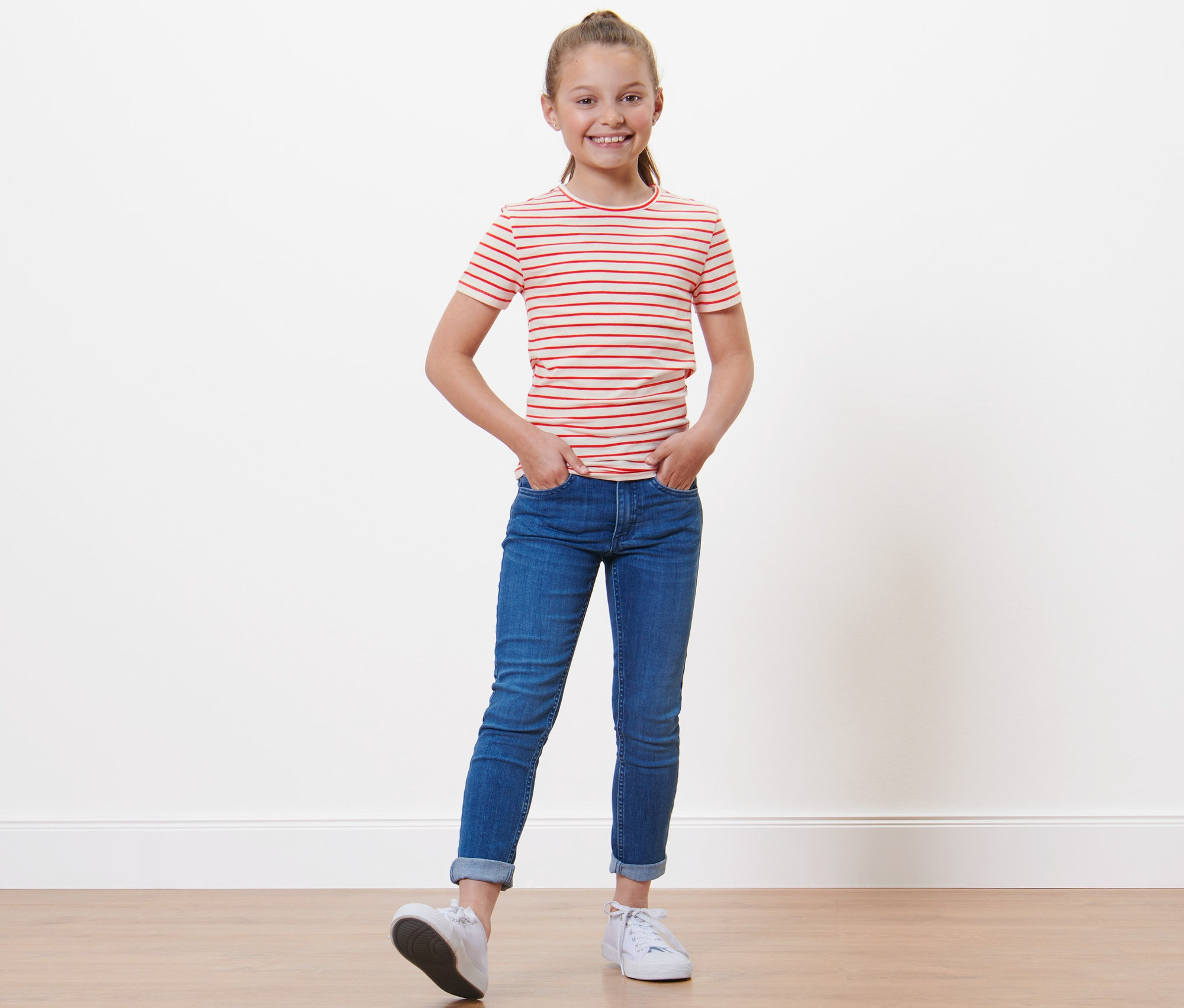 Dziewczyna w czerwono-białej koszulce w paski i dżinsach stoi z rękami w kieszeniach. Koszulki, 3 sztuki.