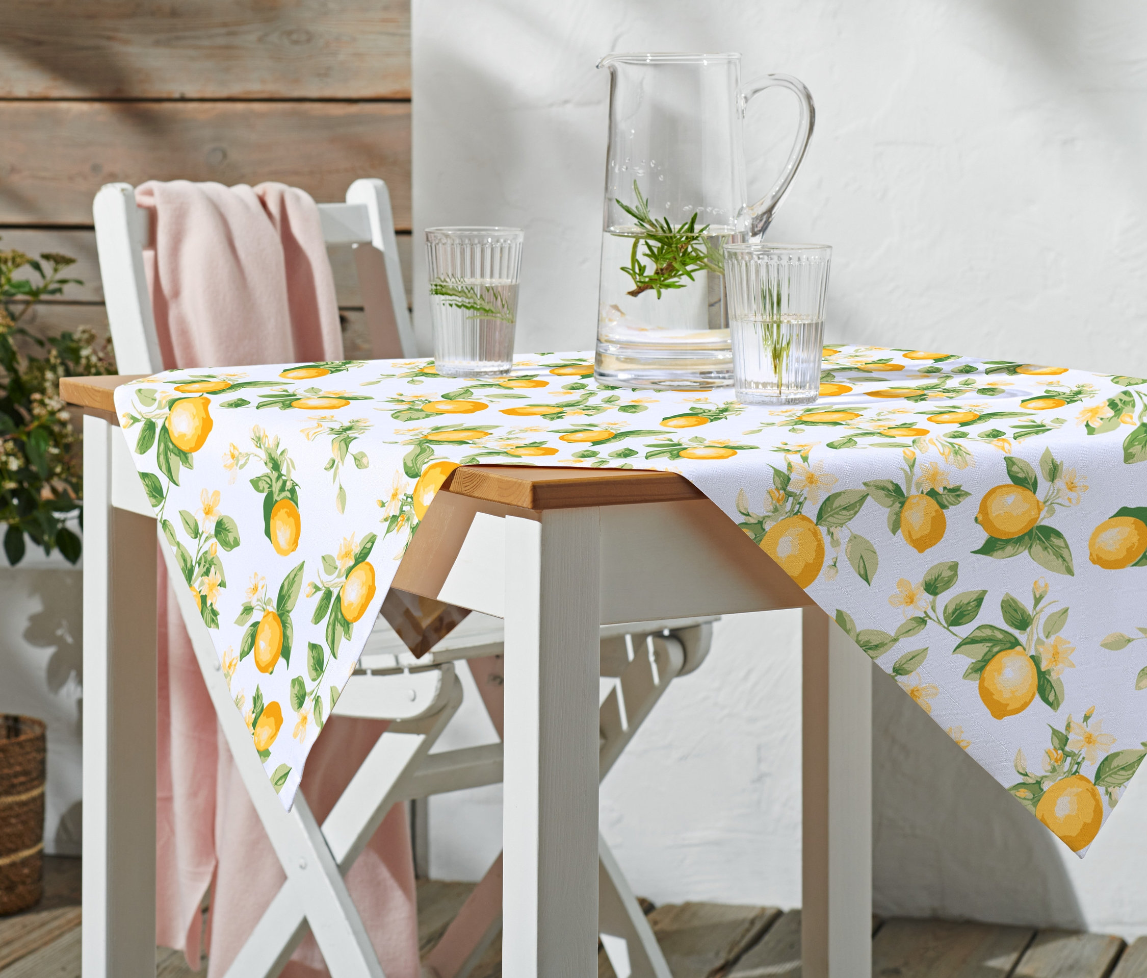 Stół z obrusem bawełnianym w cytryny, szklankami i dzbankiem wody stoi na zewnątrz.