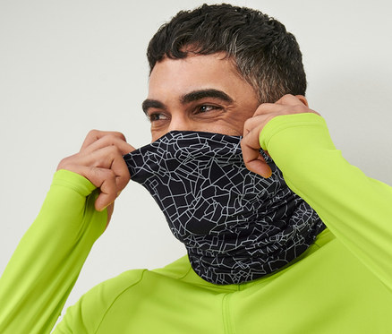 Mężczyzna naciąga na twarz czarną, odblaskową chustę wielofunkcyjną.