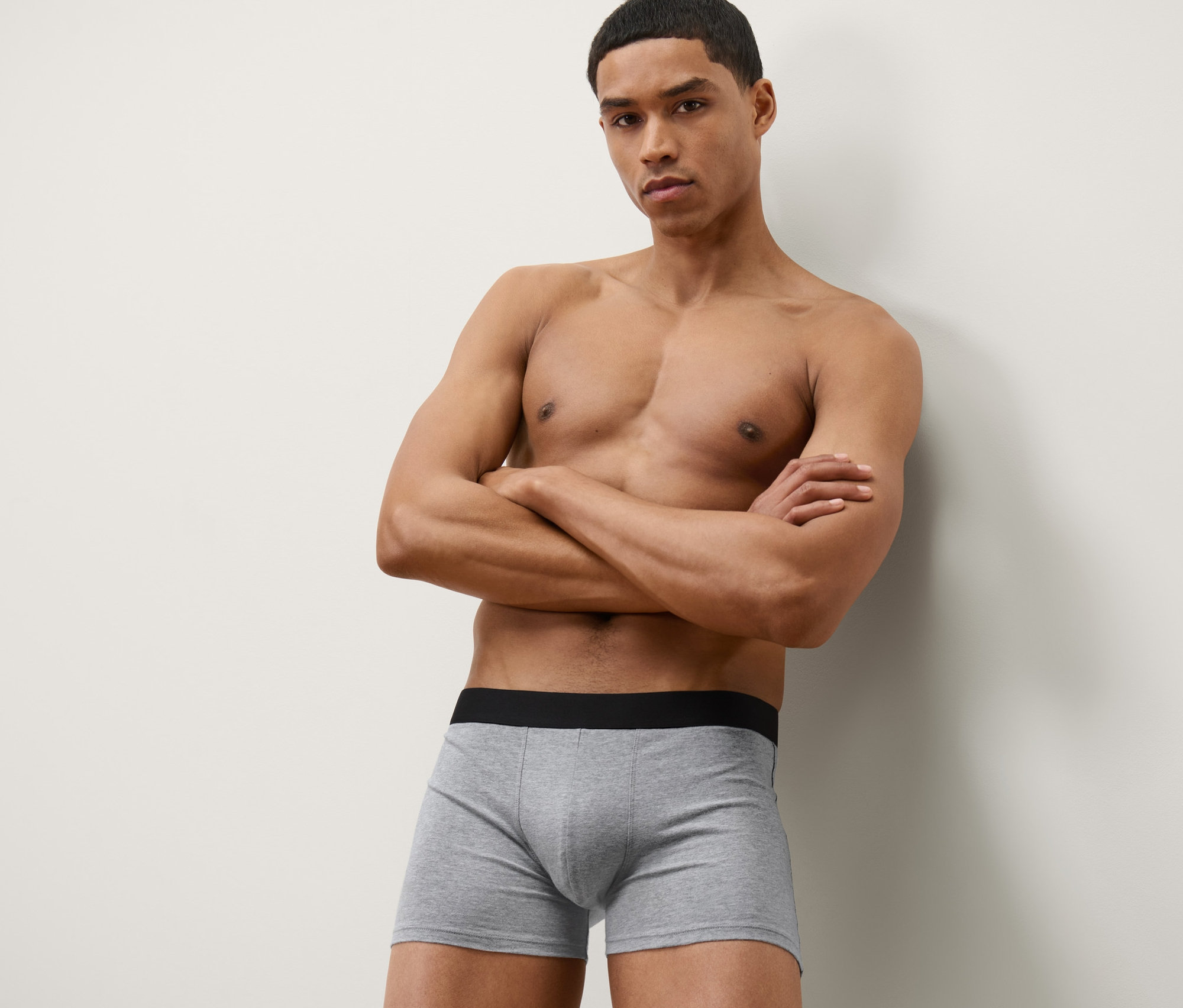 Mężczyzna pozuje ze skrzyżowanymi ramionami w szarych bokserkach, 4 pary.