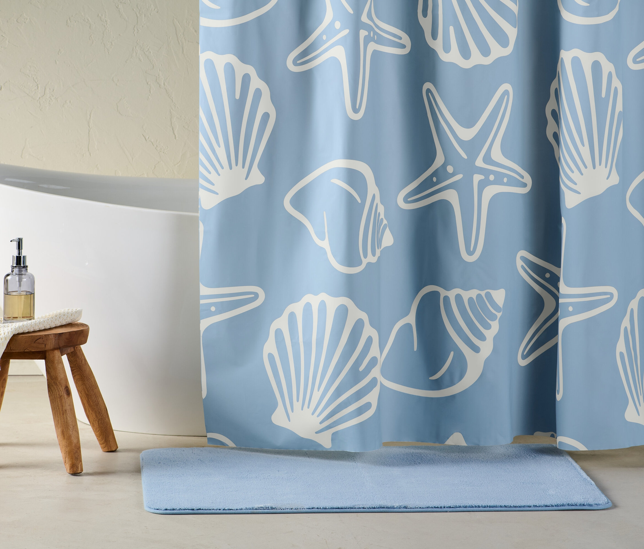 Niebieska zasłona prysznicowa z białymi rozgwiazdami i muszlami. Obok wanny stoi stołek z dozownikiem mydła.