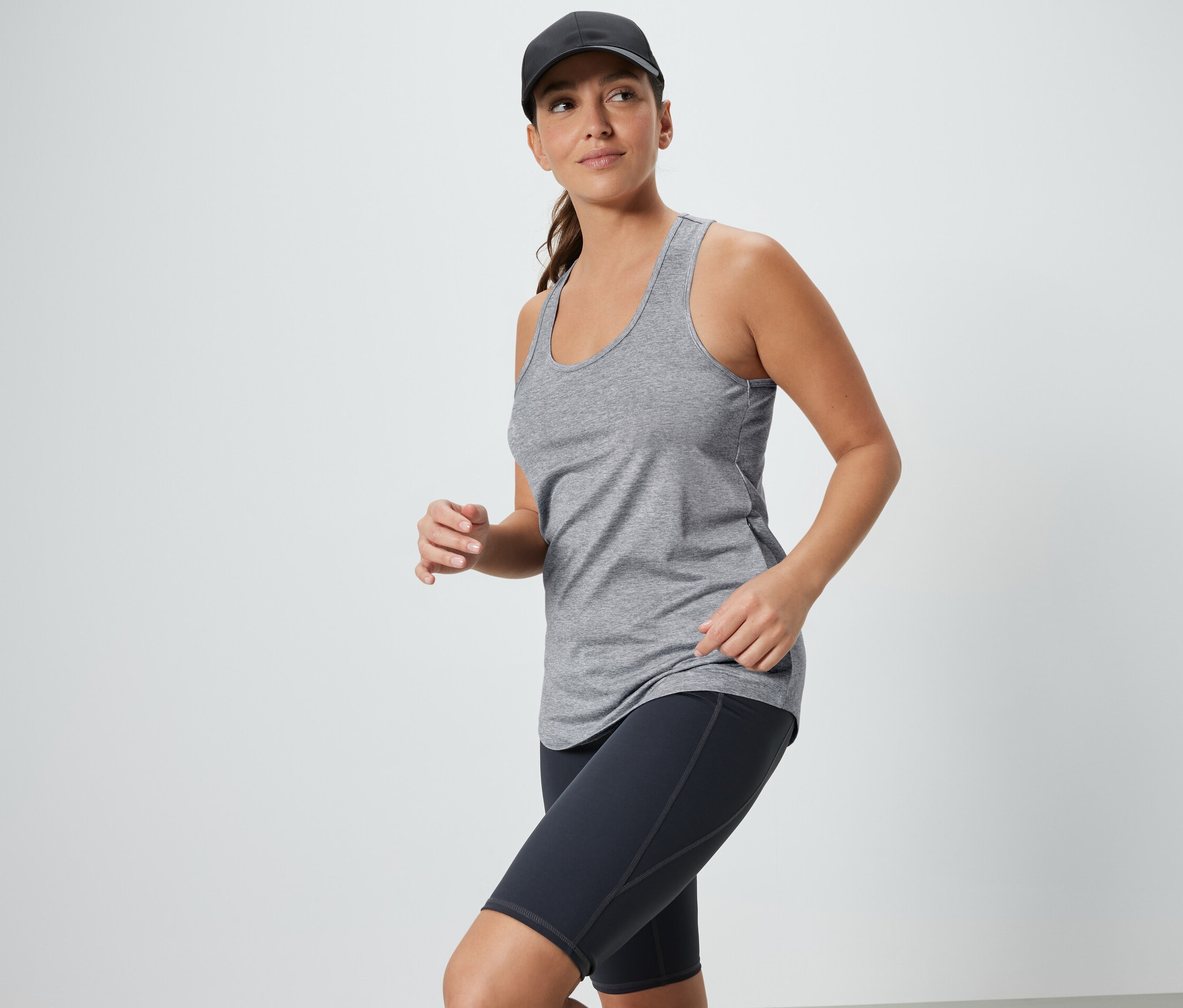 Kobieta w szarym topie i czarnych szortach sportowych z czapką z daszkiem. Topy funkcyjne, 2 sztuki, czarny i szary.