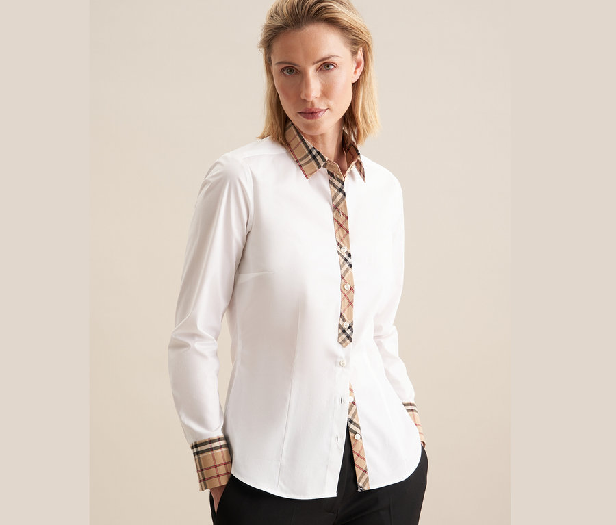 Kobieta ma na sobie białą popelinową koszulę Seidensticker z detalami w kratę.