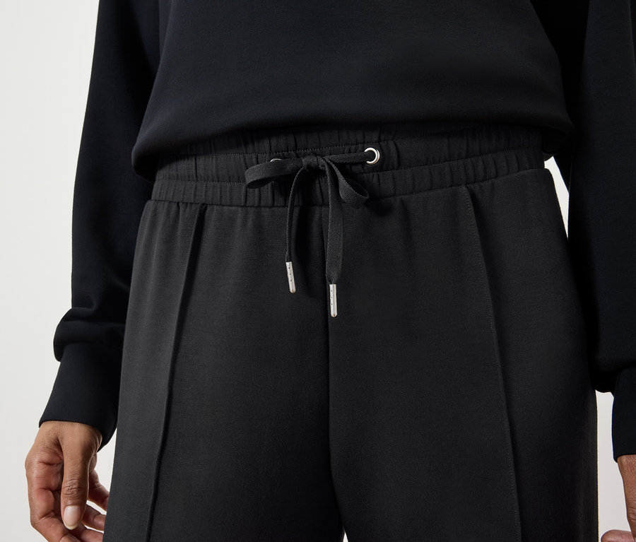 Zbliżenie na kobietę ubraną w czarne spodnie ze sznurkiem i czarny sweter.