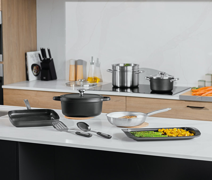 Różne garnki, patelnie i przybory kuchenne na białym blacie kuchennym.