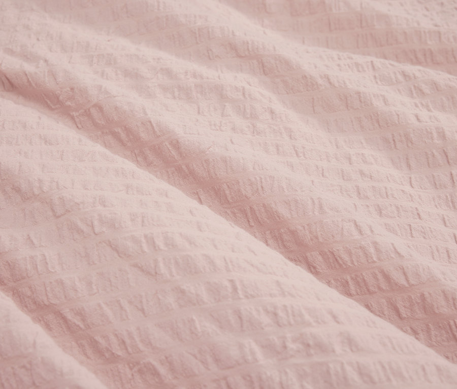 Zbliżenie na teksturowaną, jasnoróżową tkaninę.
