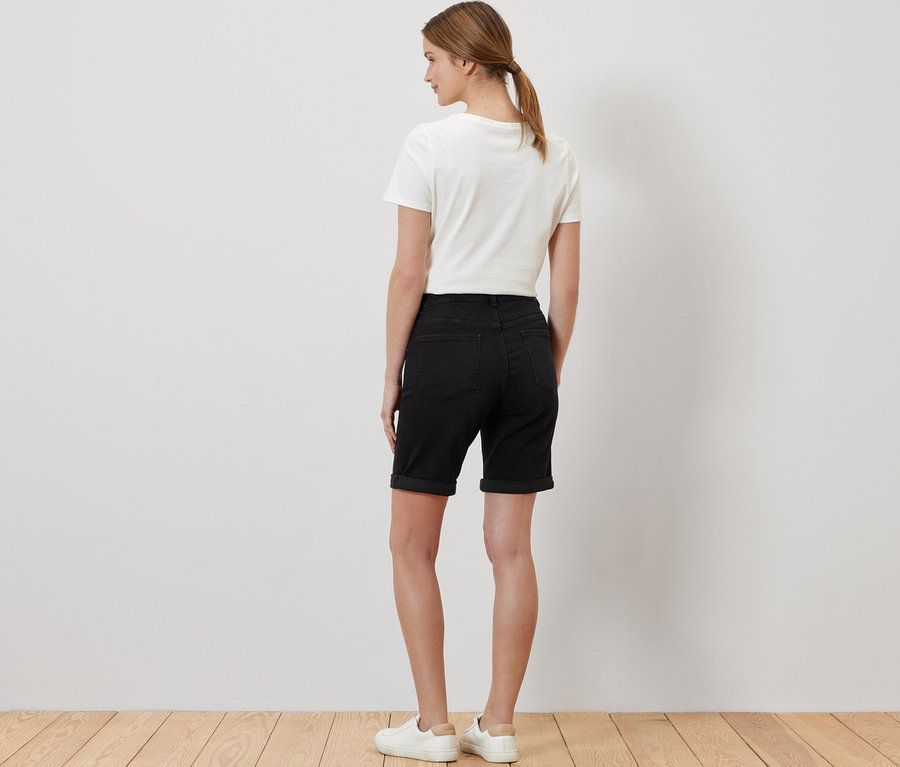 Kobieta stoi tyłem w dżinsach bermudach – fason „Lea”, black denim, białym T-shircie i tenisówkach.