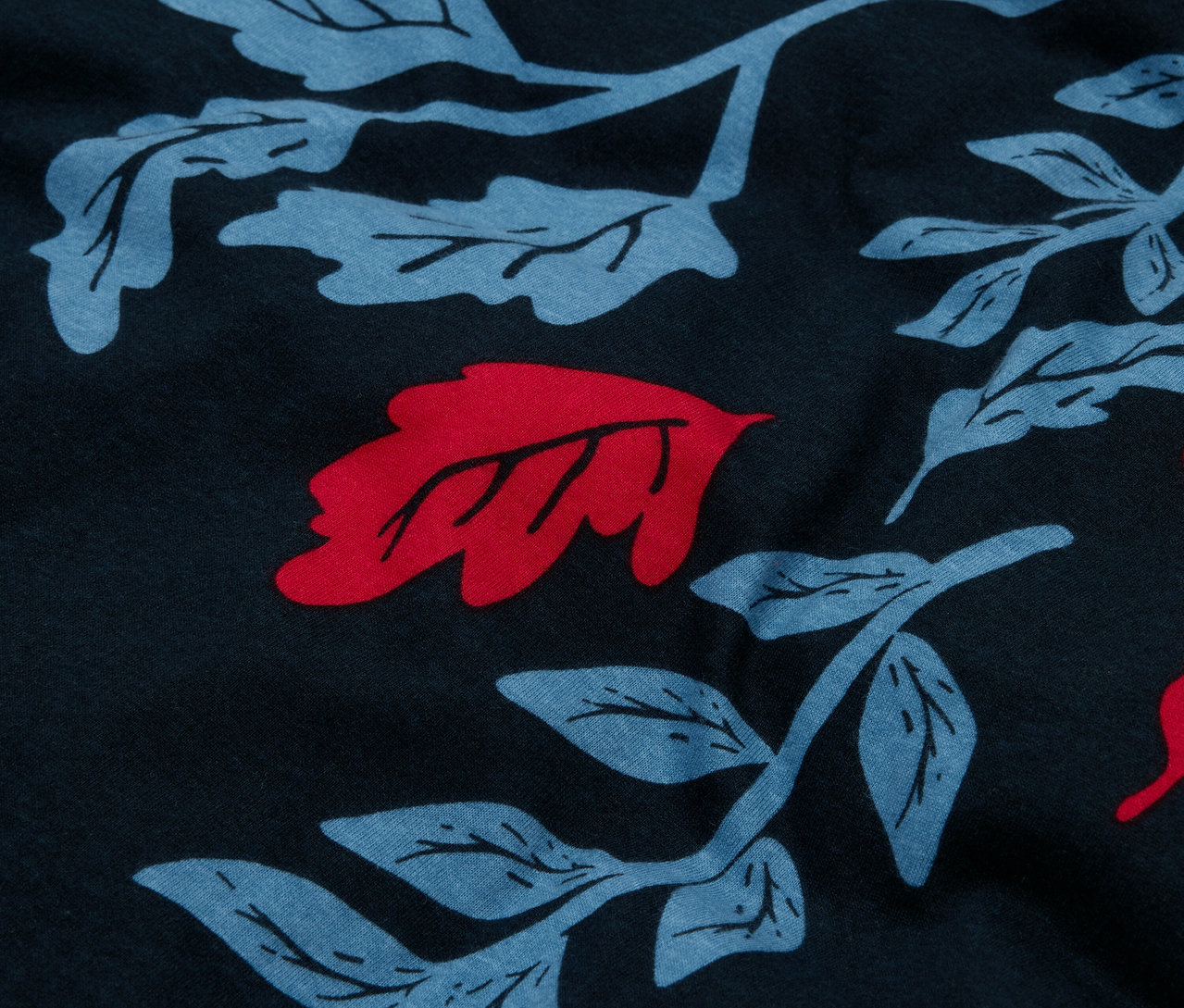 Zbliżenie na granatowy materiał z wzorem niebieskich liści i czerwonymi akcentami.