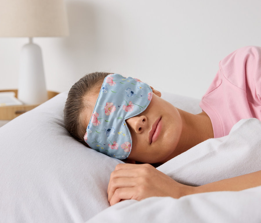 Kobieta śpi w łóżku w masce do spania w kwiatowy wzór.