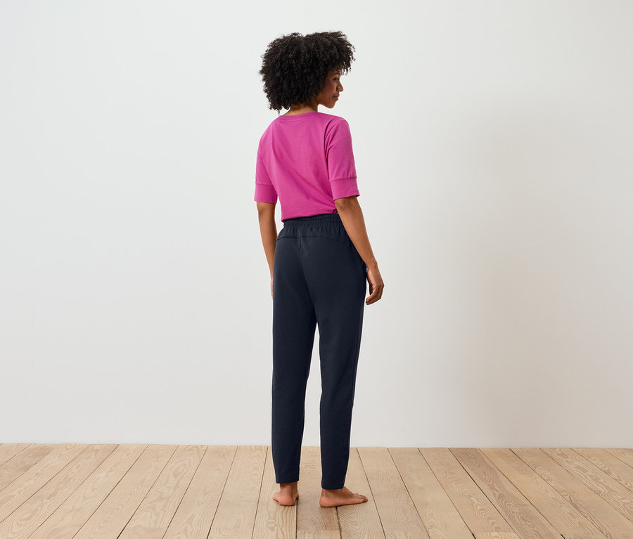Widok z tyłu na kobietę z afro, ubraną w różowy t-shirt i granatowe spodnie.
