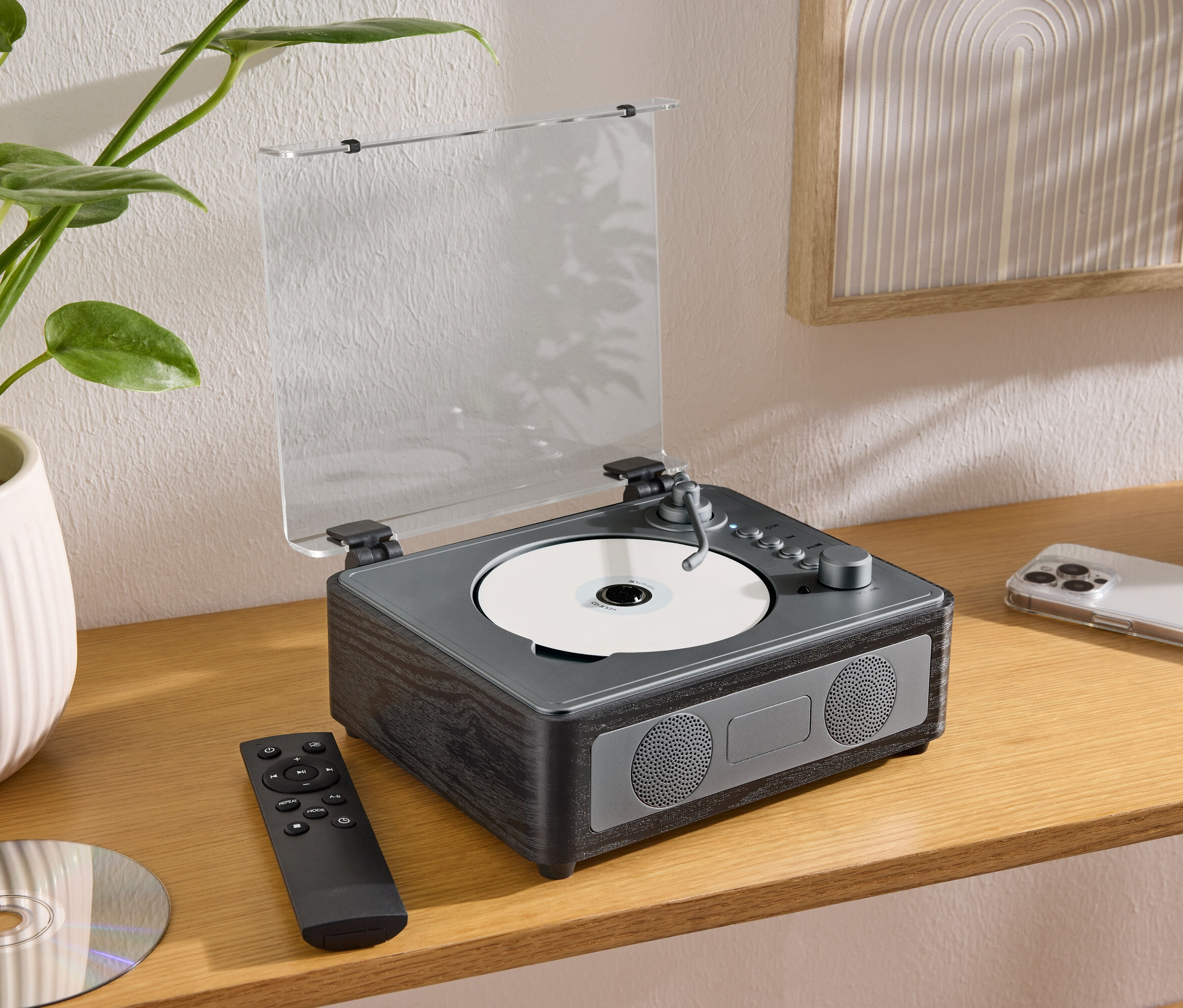 Na stole stoi głośnik CD/Bluetooth® z płytą CD, pilotem i telefonem komórkowym.